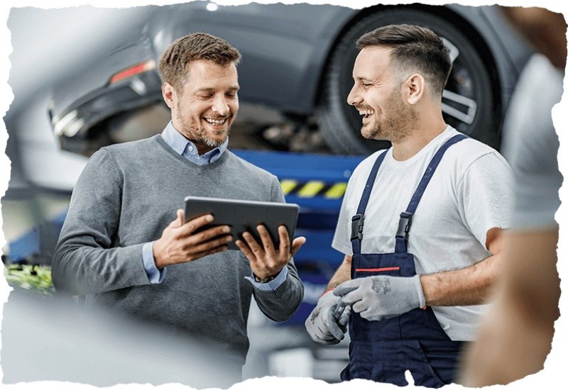 Happy customer and auto mechanic using a touchpad in a workshop in the garage by the Tire Pirates in Calgary, AB